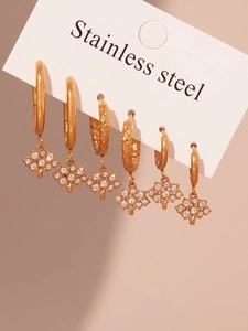 Détail de six boucles d'oreilles créoles en acier doré avec pendentifs arbre de vie et cristal