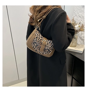 Detail of leopard print underarm bag with leather trim and gold buckle worn by model