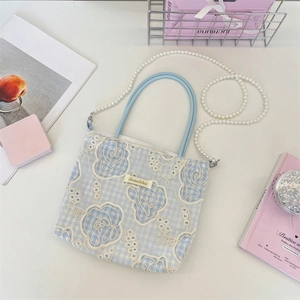 Détail du sac à carreaux bleus avec dentelle florale blanche et chaîne de perles élégante