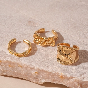 Detailed view of three gold liquid-metal rings with irregular textured folds on stone