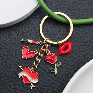 Golden keychain with red cartoon lipstick, rose, and heart charms on black leather surface