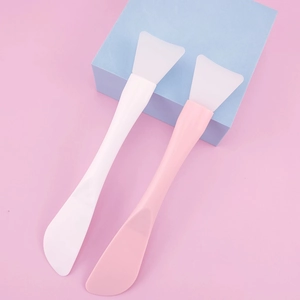 Close-up of pink and white silicone face mask brushes on a blue geometric prop background