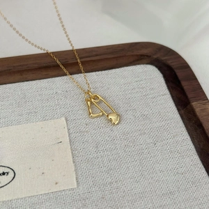 Elegant gold heart safety pin and geometric double pendant necklace on a wooden tray