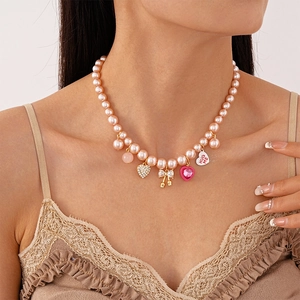 Détail du ras-du-cou en perles roses avec cœur en strass et nœud doré