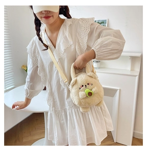 Detail of plush beige cat crossbody bag holding an avocado accessory with soft texture