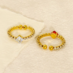 Detailed view of adjustable gold-finish rings with square crystal accents on textured surface