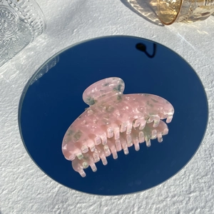 Detailed top view of a pink marble acetate hair claw clip reflecting on a round mirror