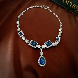 Detailed flat lay of silver necklace with deep blue gems on luxurious silk fabric