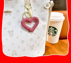 Detailansicht des pinkfarbenen Herzanhängers mit Strass an einer weißen Handtasche