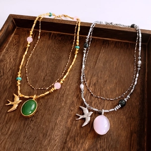 Gros plan de colliers vintage double couche avec pendentifs hirondelle sur plateau