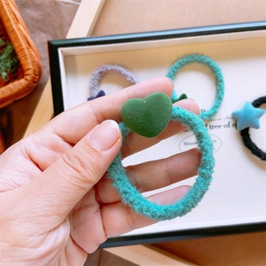 Dettaglio dell'elastico per capelli peluche turchese con un ciondolo a cuore verde