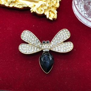 Detailed view of a gold-toned dragonfly brooch with rhinestones and black gemstones on velvet