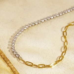Asymmetric gold and silver chain necklace with sparkling crystals on natural stone background