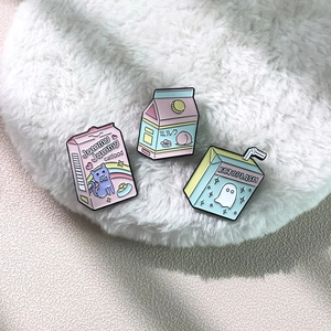Detail view of cute milk box and snack enamel pins on soft white faux fur background