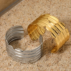Wide textured stainless steel open bangles in gold and silver finish on sand background