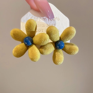 Macro shot of yellow flocked flower earrings with blue bead center on display card