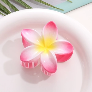Detailed top view of a realistic pink plumeria hair claw clip on a tropical green leaf