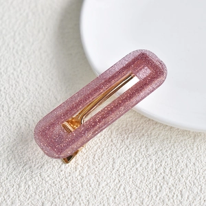 Detailed macro shot of a sparkling pink glitter acetate rectangular hair clip with gold metal base