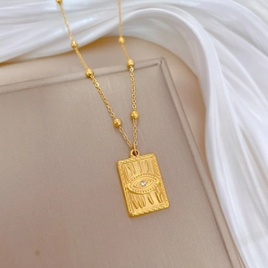 Gold Evil Eye necklace with rectangular pendant on a beige book and white silk background