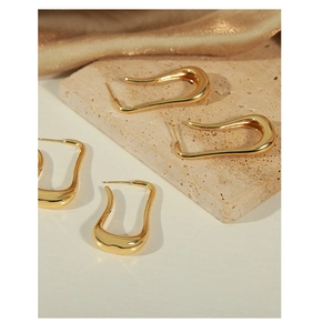 Artistic layout of golden U-shaped geometric earrings on beige stone and silk fabric