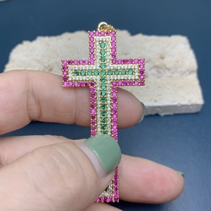 Close-up of 18k gold cross pendant featuring red, green, and white zircon gemstones