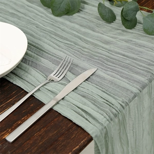 Close-up of sage green crinkle cheesecloth table runner with natural texture, wedding decor detail.