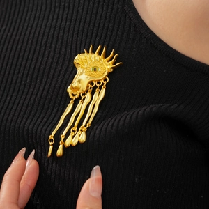 Close-up of a vintage golden eye brooch with green texture and long hanging tassels