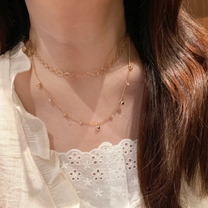 Dettaglio di collana dorata a strati con pendente a cuore e cristalli su camicia di pizzo