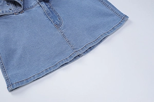 Detailed macro view of denim skirt hem with precise stitching and metal eyelet belt detail