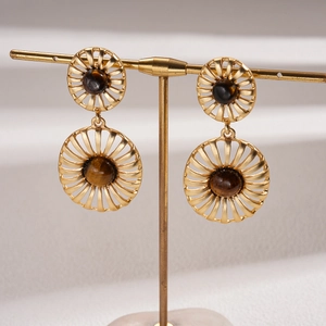 Macro shot of gold oval earrings with radial cutout design and brown tiger eye stone