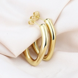 Macro shot of gold U-shaped titanium earrings on soft pink silk background
