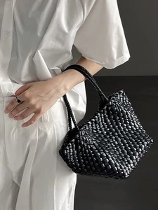 Detail of a black hand-woven tote bag held by a model in a white outfit for contrast