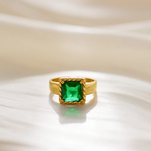 Close-up of golden ring with emerald-cut green stone and twisted rope edge detail