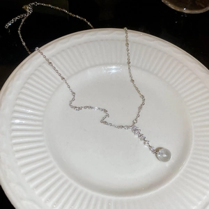 Detail of zircon pendant necklace featuring a clear spherical bead on a white ceramic plate