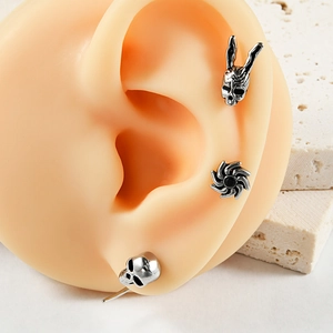 Retro stainless steel stud earrings with skull and mask designs on a display model