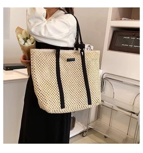 Detail of hollow woven beige tote bag with black handles and a small square logo patch