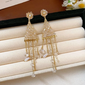 Détail de boucles d'oreilles fleuries dorées avec pompons et cristaux en écrin