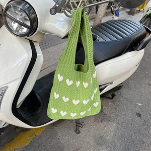 Detail of green knitted tote bag with white heart patterns hanging on a bike handle