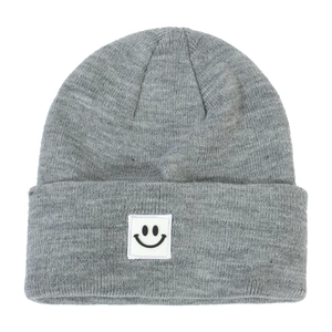 Close-up of gray knitted beanie showing textured yarn and square smiley face patch