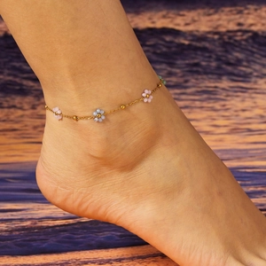 Close-up of gold anklet with colorful flower beads on an ankle at sunset beach