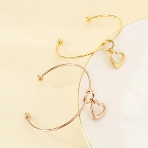 Detailed close-up of 18K gold and rose gold hollow heart pendants on knot open bangles