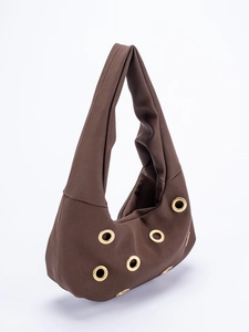 Close-up of suede shoulder bag with decorative gold metal eyelets in dark brown