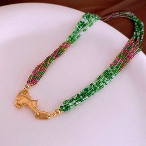 Detail of multi-layer beaded necklace with golden leopard clasp on white plate
