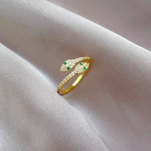 Detail of gold snake ring with green gem eyes and white zircon stones on silk fabric