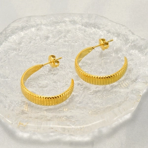 Classic gold stainless steel C-shaped earrings with textured stripe design on white silk