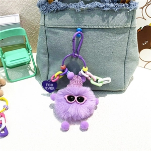 Détail du porte-clés peluche violette avec lunettes sur un sac en jean bleu