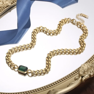 Gouden Cubaanse schakelketting met vierkante groene kristal op een vintage spiegel