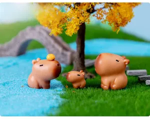 Close-up of cute capybara resin figurines in a miniature garden with a tiny orange decoration