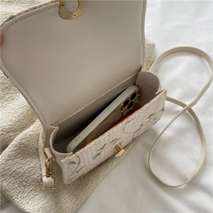 White woven straw crossbody bag with green floral embroidery and smartphone inside