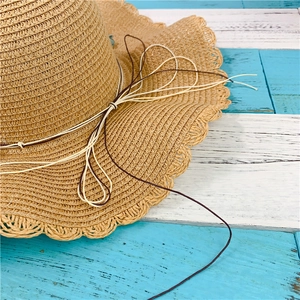 Close-up of woven straw hat with wavy scalloped edge and decorative cord detail